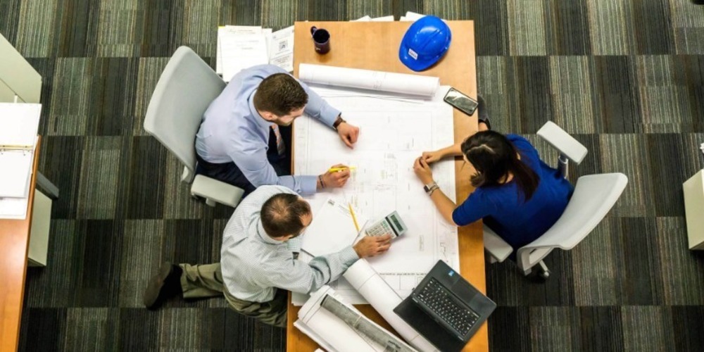 Three Workers Communicating Around a Table in the Construction Industry